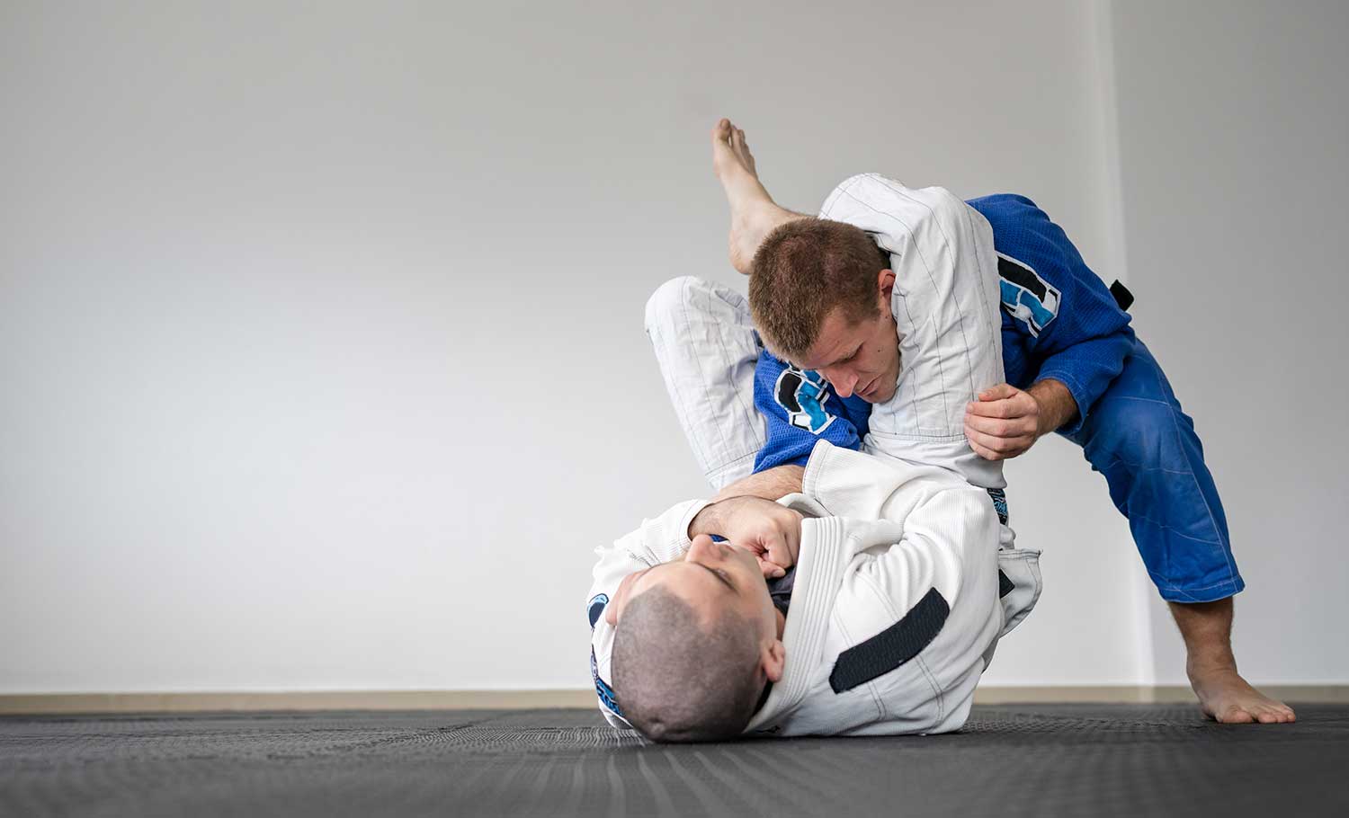 Two Jiu-Jitsu competitors practicing on the mat inside a gym