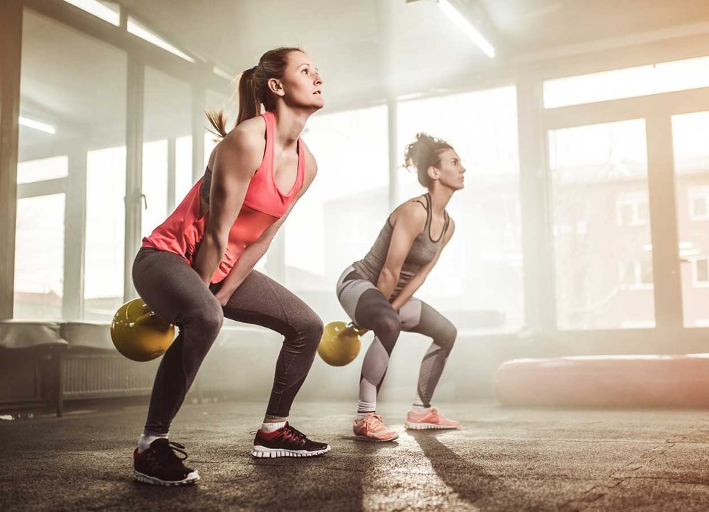 Two women in a gym doing kettlebell swings.