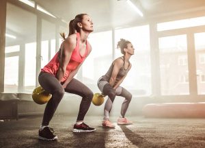 Two women in a gym doing kettlebell swings.